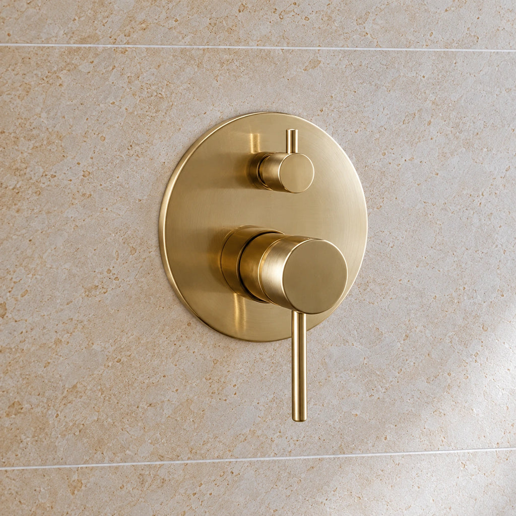 Détail de la commande ronde ORIO DUO or brossé OLVERTON, fixée sur le mur en pierre de la douche.