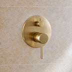 Détail de la commande ronde ORIO DUO or brossé OLVERTON, fixée sur le mur en pierre de la douche.