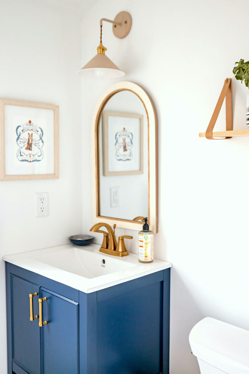 Meuble de salle de bain bleu marine, mitigeur en laiton et miroir arqué