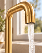 Gros plan du bec en or brossé et de l'aérateur du mitigeur FÄLLA, jet d'eau